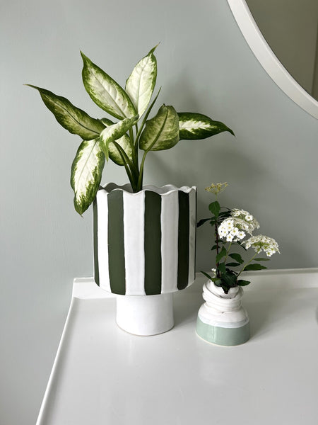 Olive green and white striped vessel or planter in bathroom setting
