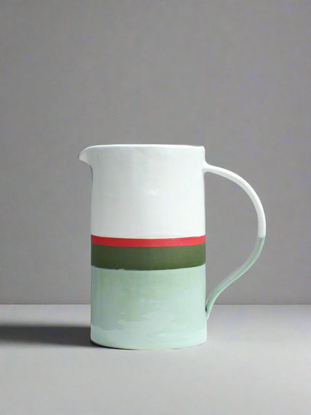 A ceramic water jug with a white gloss glaze on the top, matte green and red in the middle, and a gloss sage green on the base.