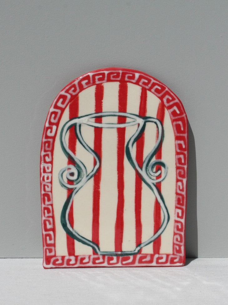 A hand painted ceramic art tile with a geometric pattern featuring red stripes and white design elements, signed by artist Susan Christie.