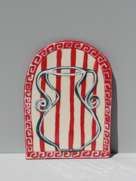 A hand painted ceramic art tile with a geometric pattern featuring red stripes and white design elements, signed by artist Susan Christie.