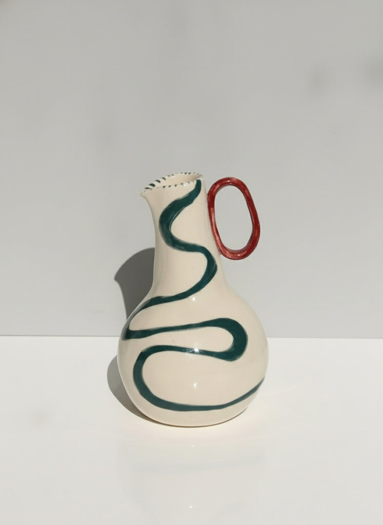 Ceramic vase with green swirl design and red handle on a white background