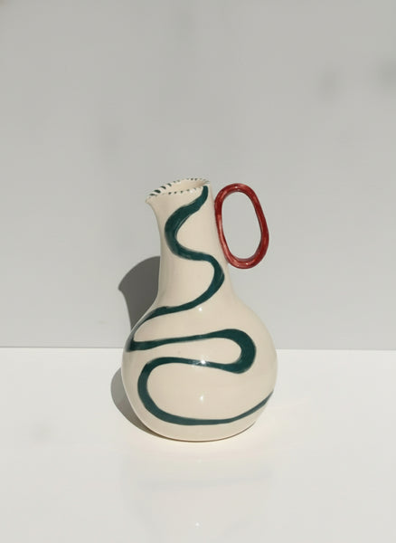 Ceramic vase with green swirl design and red handle on a white background