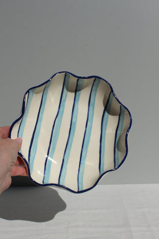 Ceramic bowl with blue and white stripes held by a hand against a gray background