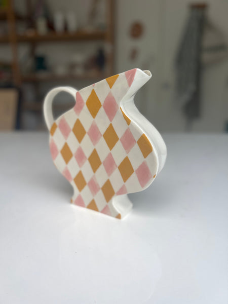 Decorative teapot with pink and gold diamond pattern on a white surface.