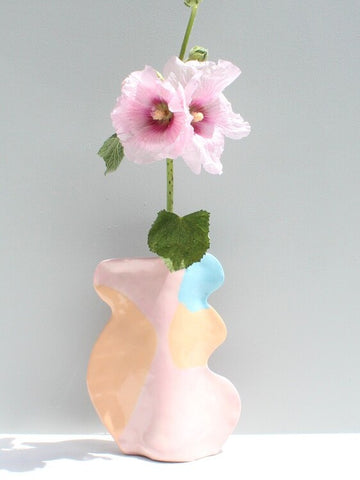 Pastel-colored vase with a pink flower on a gray background