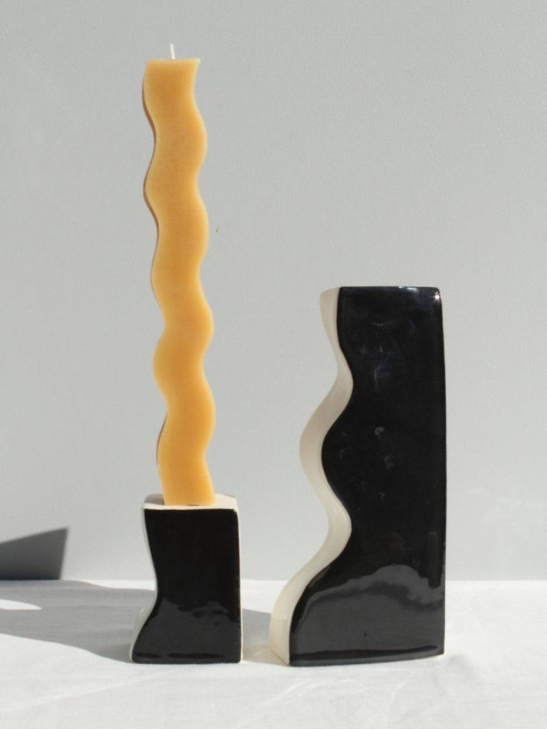 Wavy yellow candle in a black holder on a gray background