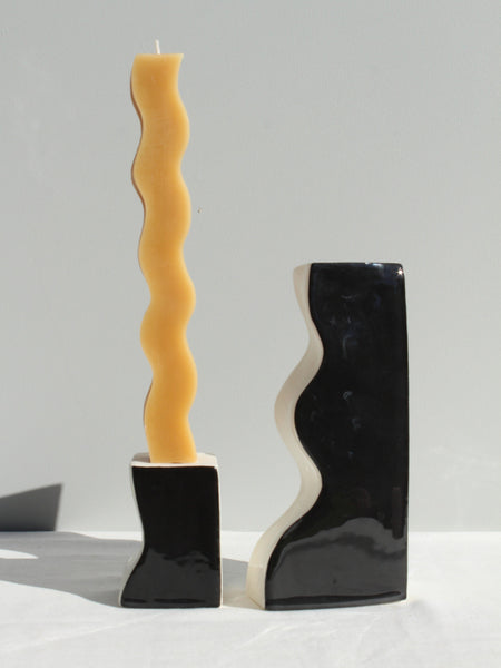 Wavy yellow candle in a black holder on a gray background