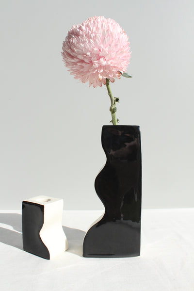 Black wavy vase with a pink flower on a white background