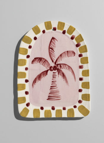 Decorative item with a palm tree design on a pink background, framed by a decorative border.
