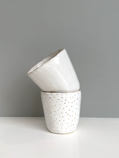 Two ceramic cups, one white with a textured surface and the other plain white, stacked on a light gray background.