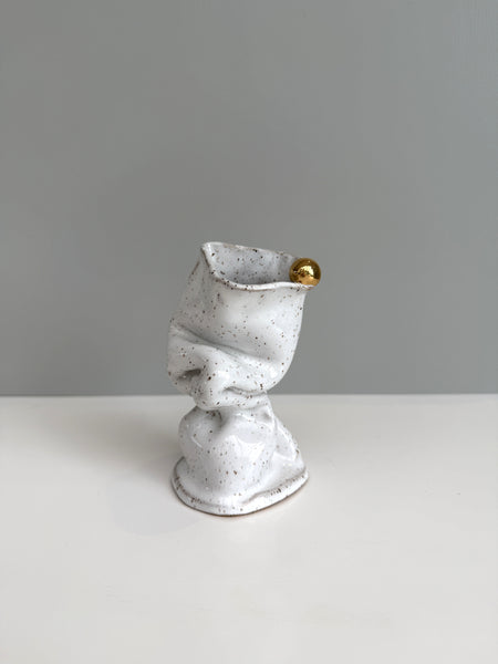 Speckled gray ceramic vase with a gold accent on a white surface and gray background