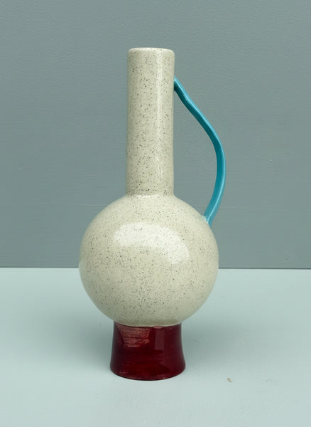 Hand holding a ceramic vase with a textured white body and red base against a gray background