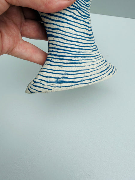 Ceramic vase with blue striped pattern held by a hand on a light gray background